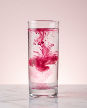 Raspberry pink CHICKSTIX powder dissolving into a glass of water